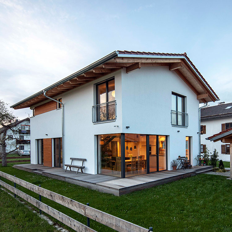 Ein modernes Niedrigenergiehaus in Tuntenhausen mit großen Fenstern und einer Holzveranda steht auf einem gepflegten Rasen.