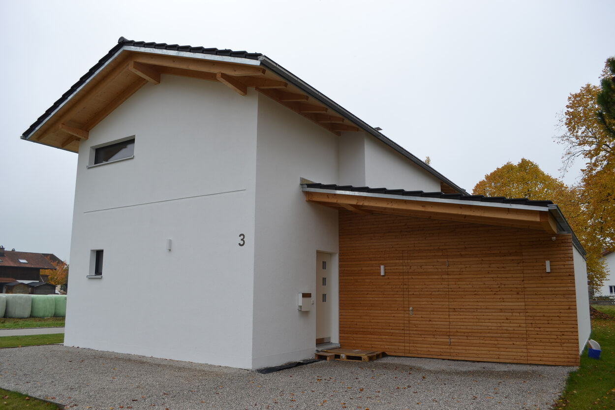 Ein modernes Passivhaus mit Holzverkleidung und weißer Fassade steht in einer ruhigen Herbstlandschaft in Übersee.