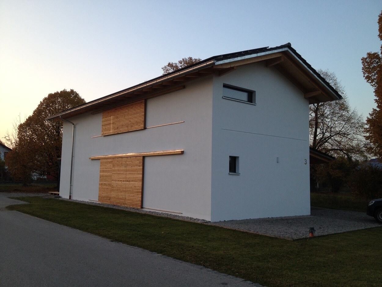 Ein modernes Passivhaus mit stilvoller Holzverkleidung steht an einer ruhigen, von Bäumen gesäumten Straße in Übersee.