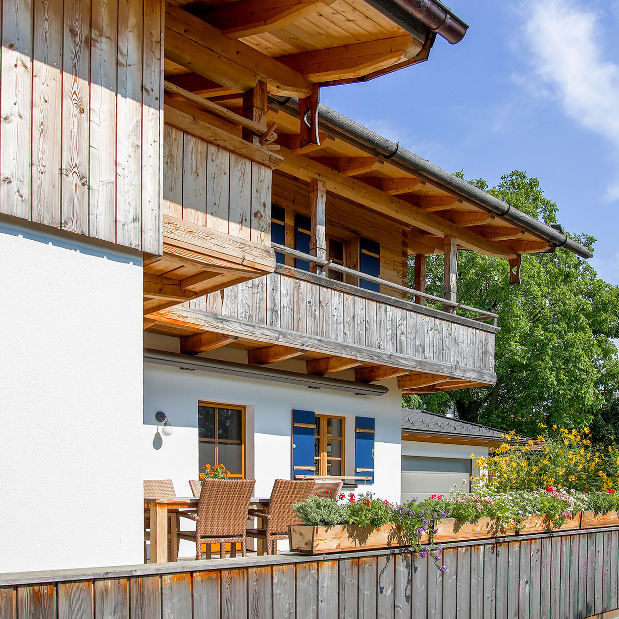 Ein modernes Wohnhaus mit Holzverkleidung und Balkon zeigt Passivhauskomponenten, umgeben von grüner Landschaft.