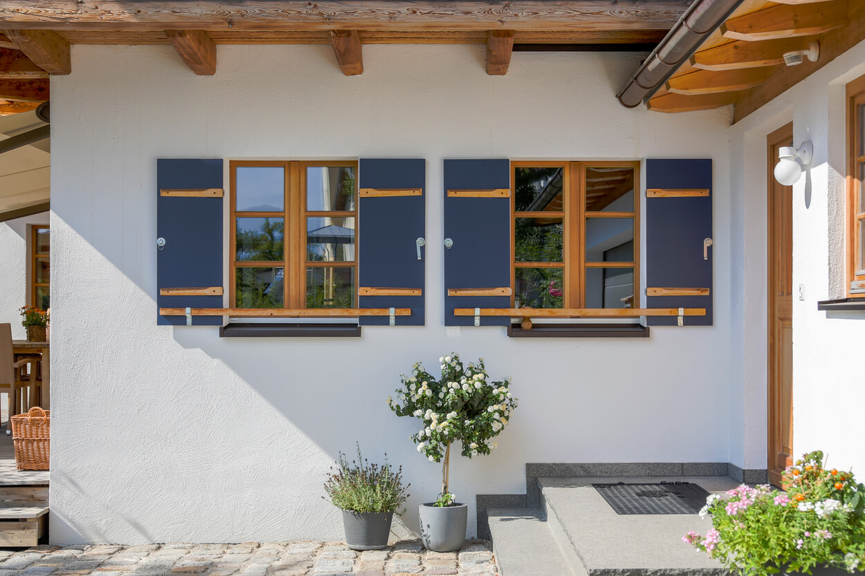 Ein modernes Wohnhaus mit blauen Fensterläden und Passivhaus-Fenstern, umgeben von blühenden Pflanzen.