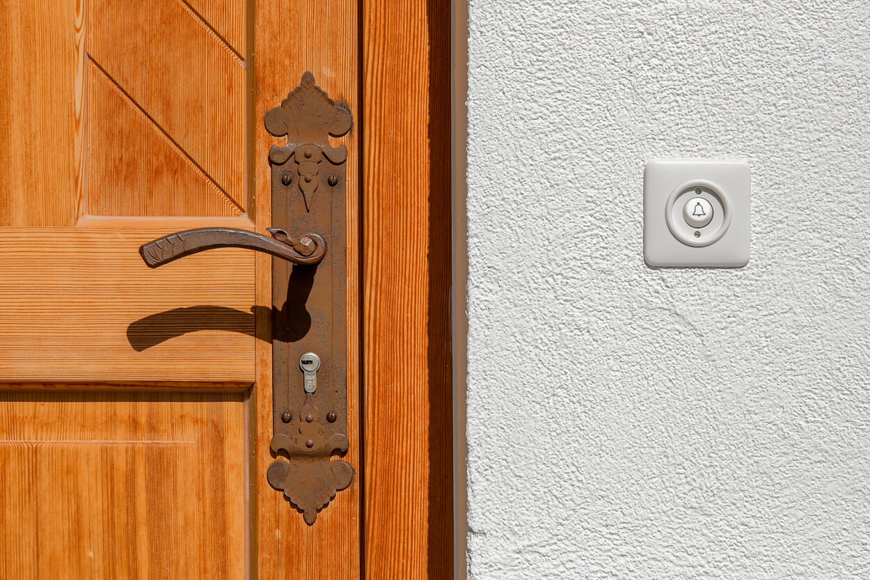 Eine Holztür mit antikem Griff neben einer weißen Wand mit Türglocke zeigt Passivhauskomponenten im Detail.