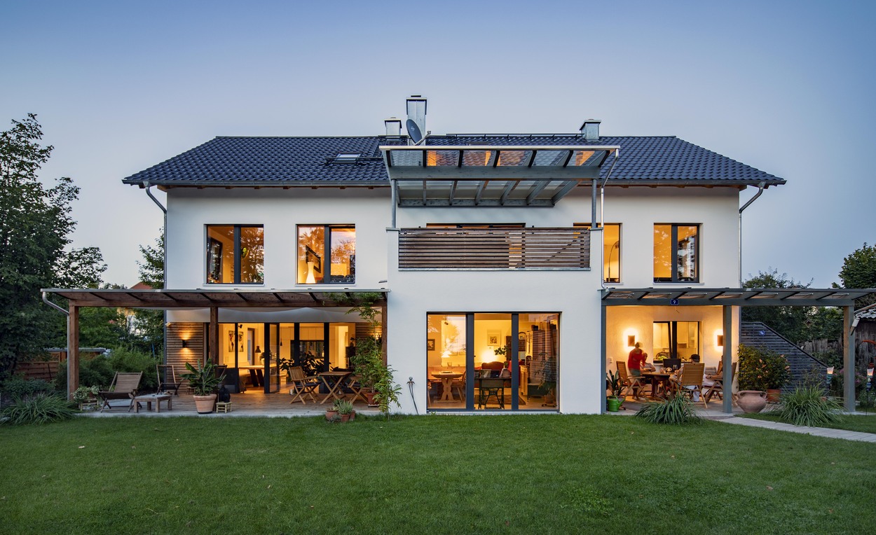 Ein modernes Mehrfamilienhaus in Kirchseeon mit beleuchteten Fenstern und gepflegtem Garten strahlt bei Abenddämmerung.