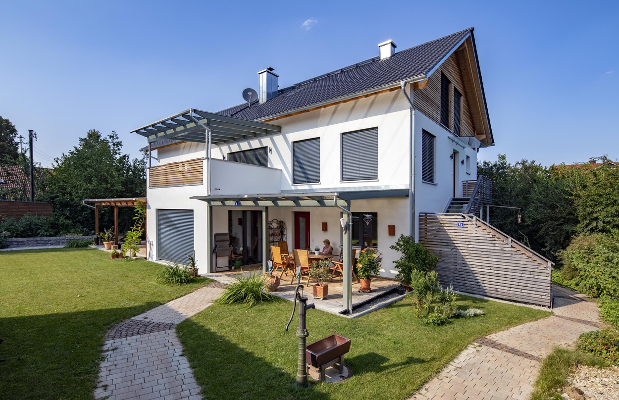 Ein modernes Mehrfamilienhaus in Kirchseeon mit gepflegtem Garten und Terrasse strahlt an einem sonnigen Tag.