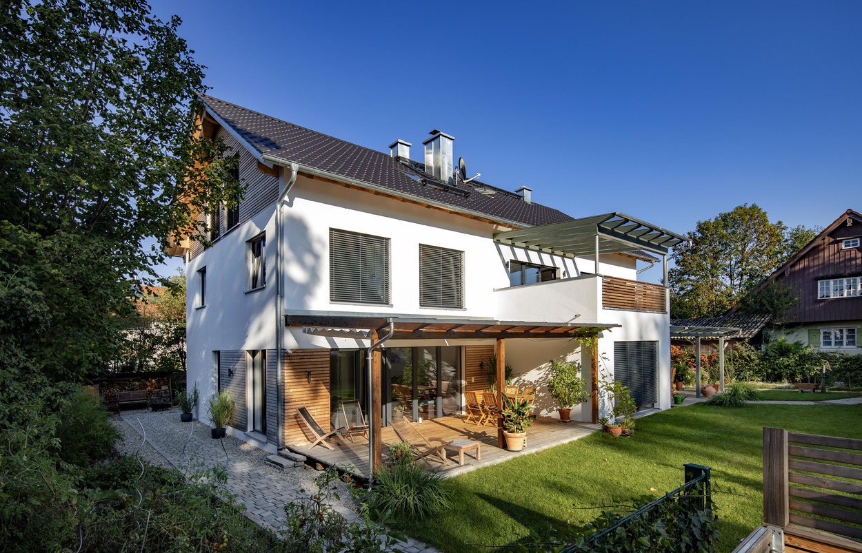 Ein modernes Mehrfamilienhaus in Kirchseeon mit gepflegtem Garten und sonniger Terrasse strahlt an einem klaren Tag.