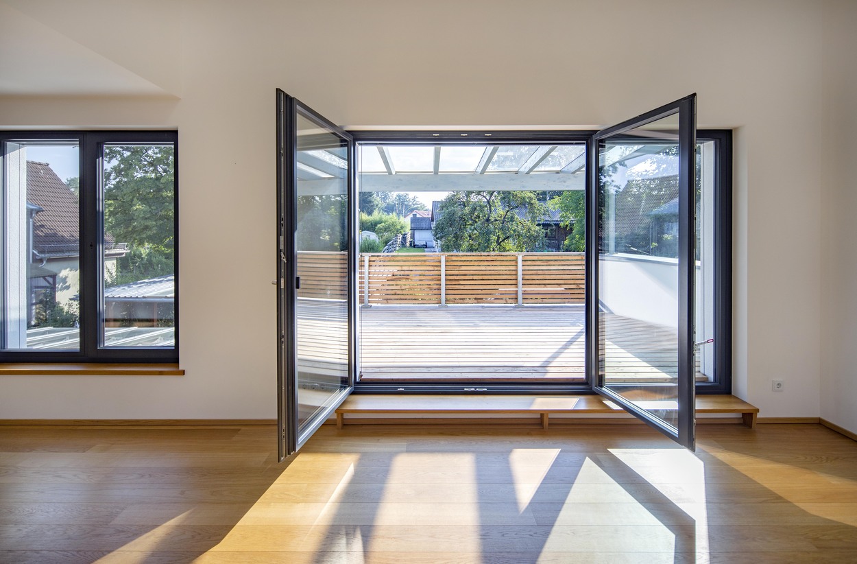 Blick von innen auf einen sonnigen Balkon mit Holzboden und umliegenden Häusern in einem Mehrfamilienhaus in Kirchseeon.