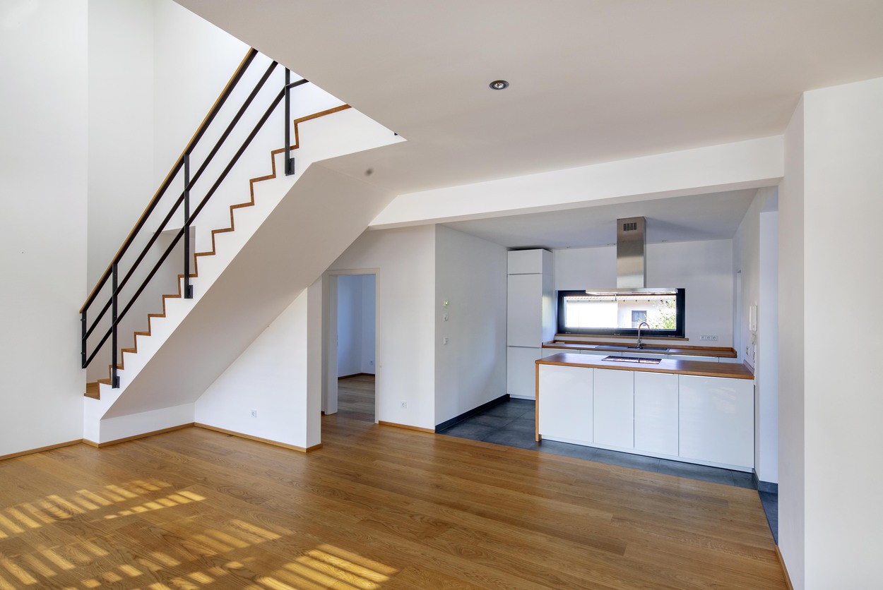 Eine moderne Küche mit Kochinsel und Holzfußboden in einem Mehrfamilienhaus in Kirchseeon liegt neben einer eleganten Treppe.