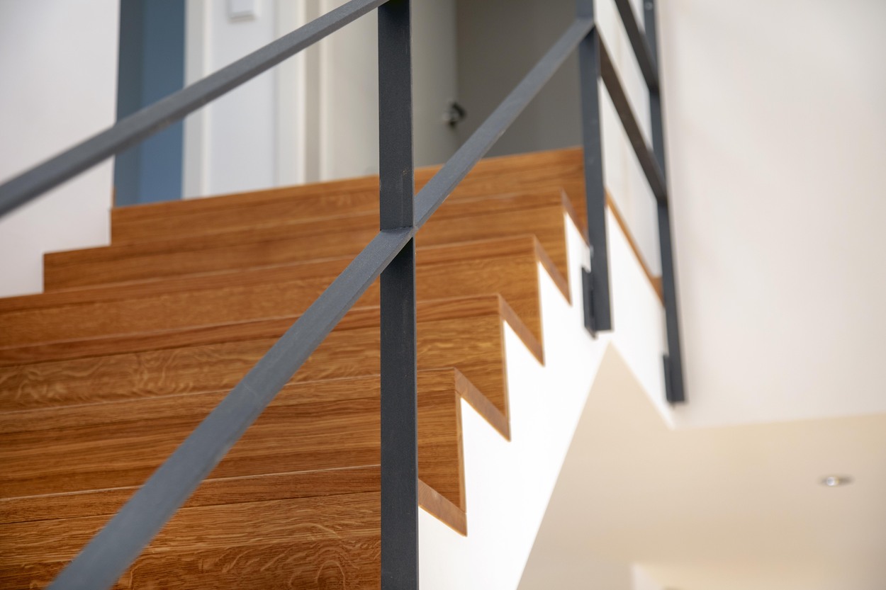 Holztreppenstufen mit schwarzem Geländer führen elegant in einem modernen Mehrfamilienhaus in Kirchseeon nach oben.