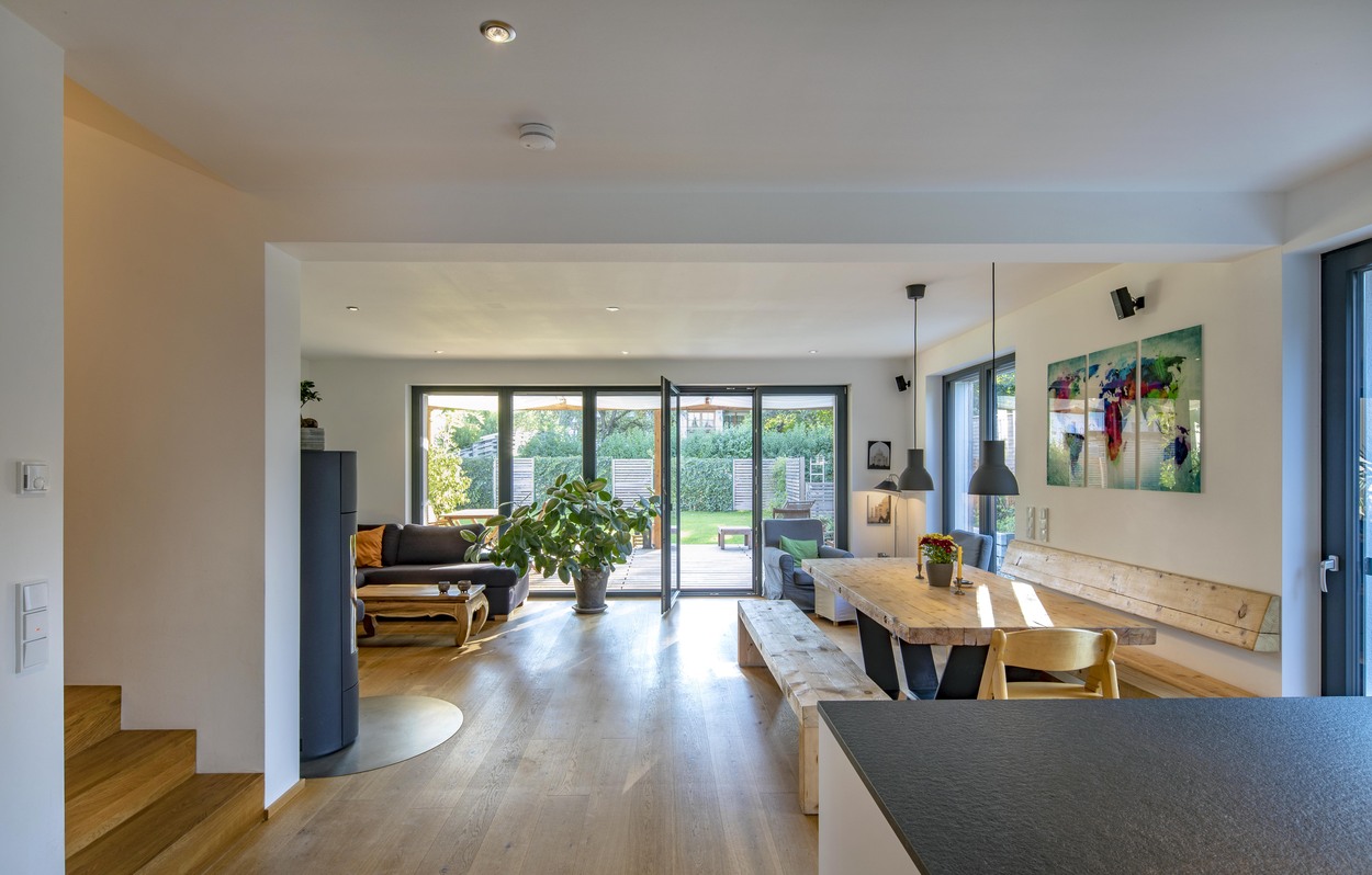 Ein offener Wohnbereich in Kirchseeon mit Holztisch, modernen Möbeln und großem Fenster bietet einen Blick auf den Garten.