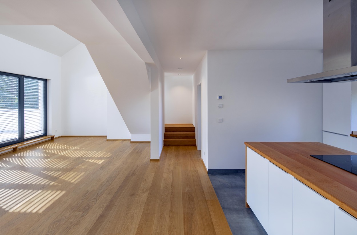 Moderner Wohnbereich in Kirchseeon mit Holzfußboden und großen Fenstern, die viel Licht in die offene Küche eines Mehrfamilienhauses lassen.