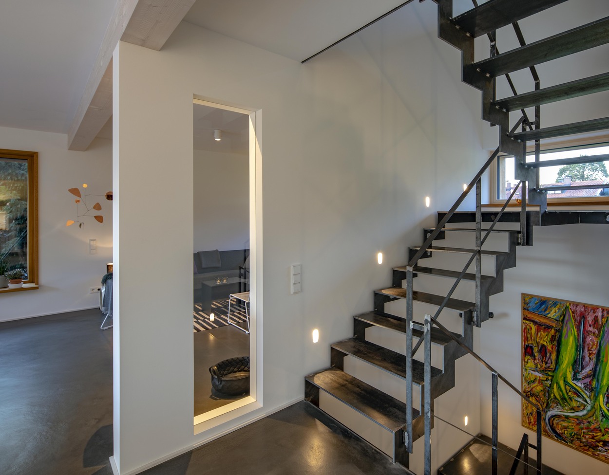 Eine moderne Treppe mit Metallgeländer führt in einem lichtdurchfluteten Holzhaus in Marquartstein nach oben.