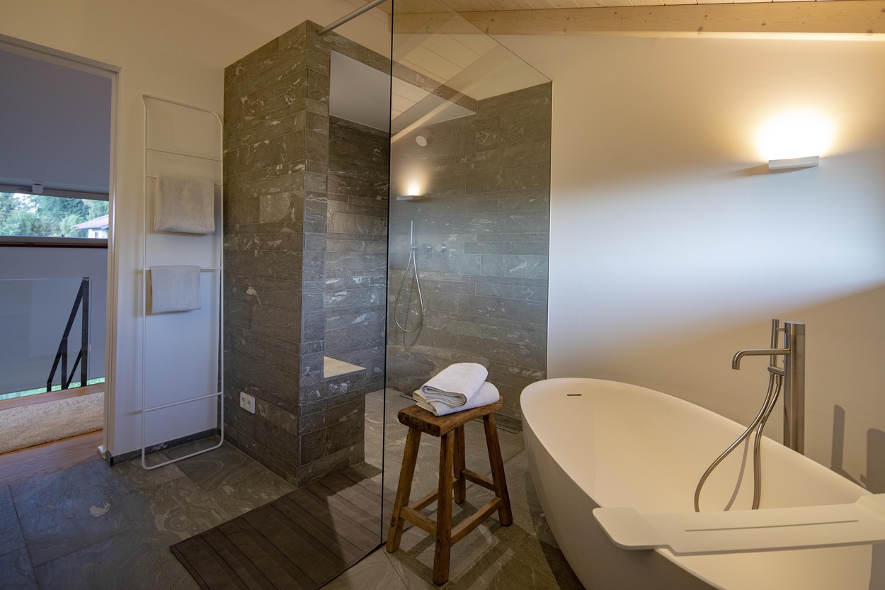 Modernes Badezimmer mit freistehender Badewanne und großer Dusche in einem stilvollen Holzhaus in Marquartstein, Chiemgau.