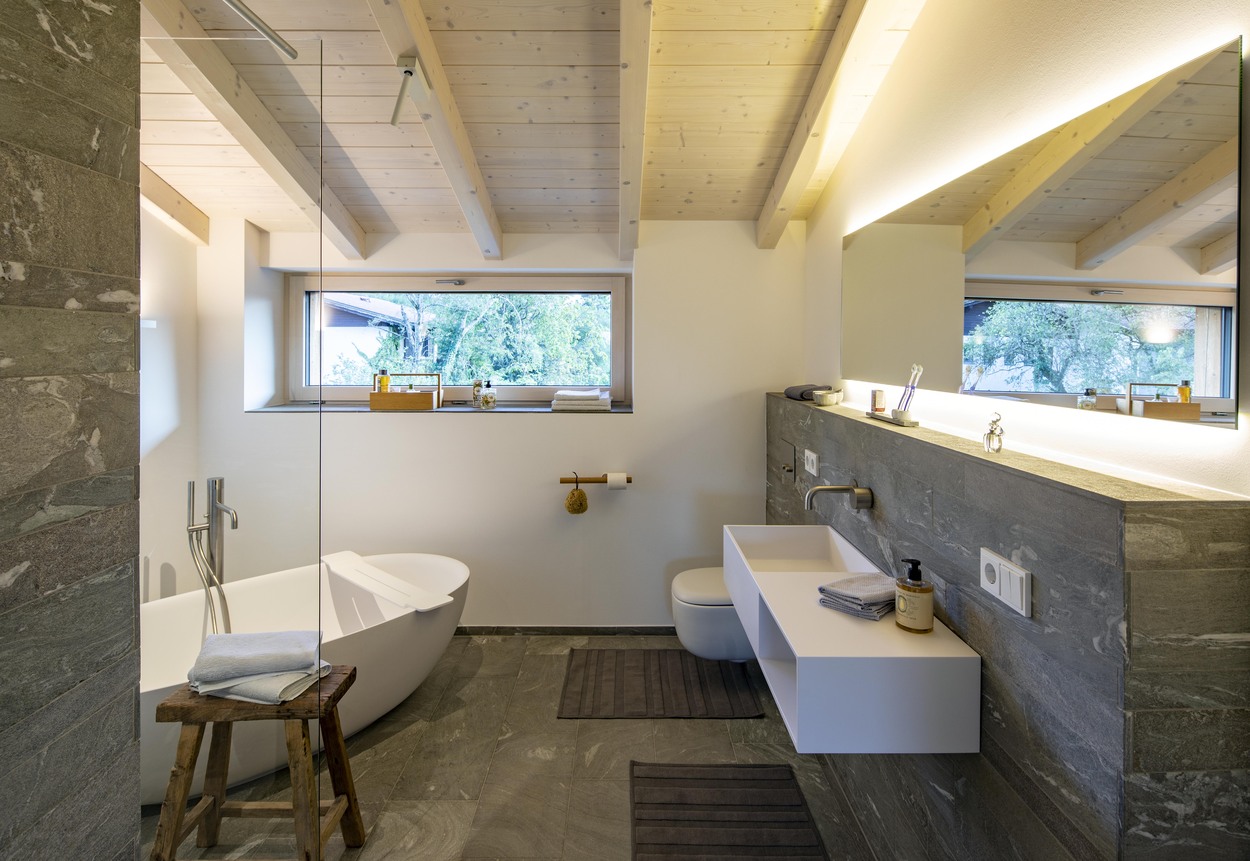 Modernes Badezimmer in einem Holzhaus in Marquartstein mit freistehender Badewanne und großem Fenster zum Chiemgau.