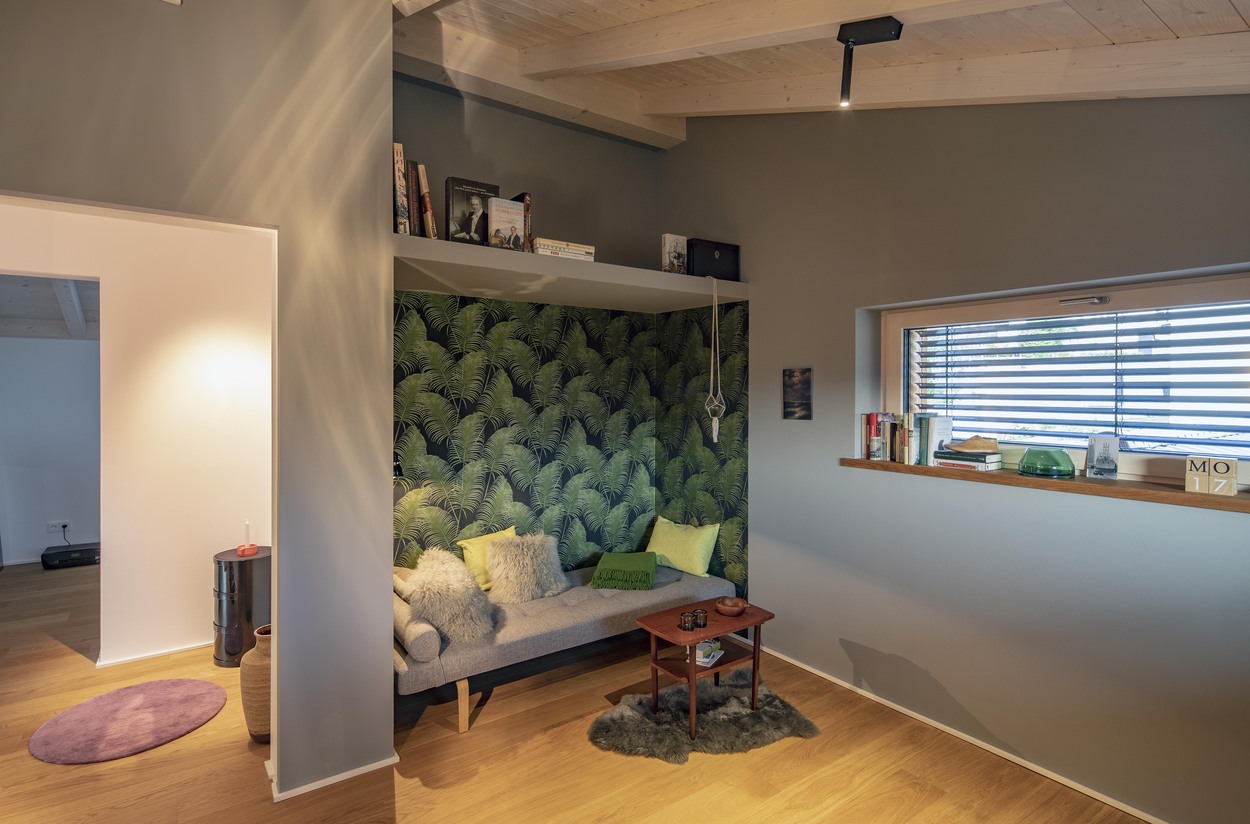 Gemütliche Sitzecke in einem Holzhaus in Marquartstein mit grüner Tapete, Sofakissen und einem kleinen Holztisch.