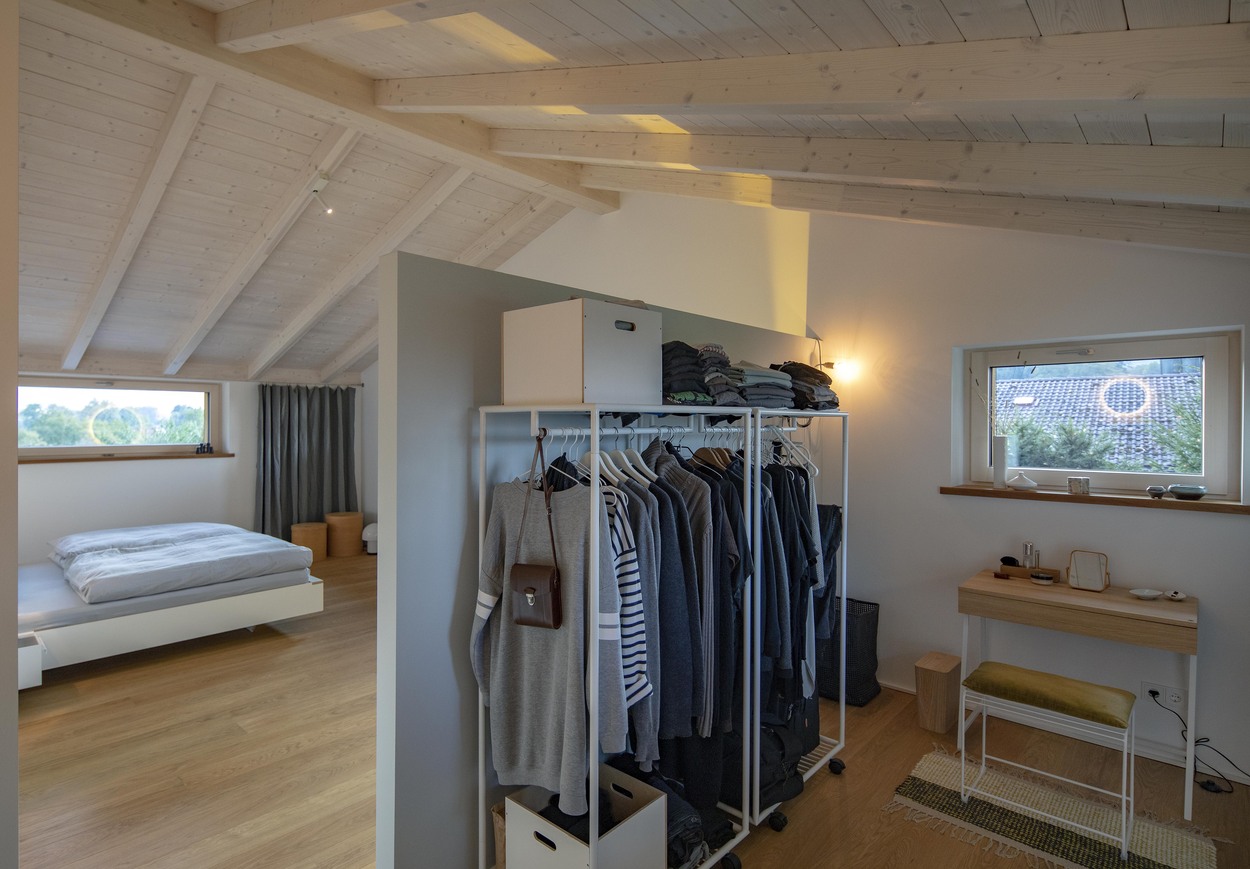 Ein modernes Schlafzimmer in einem Holzhaus in Marquartstein zeigt einen offenen Kleiderschrank und Schreibtisch unter einem Dachfenster.