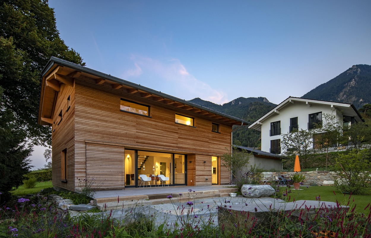 Ein modernes Holzhaus in Marquartstein, Chiemgau, steht vor einer malerischen Bergkulisse bei Dämmerung.