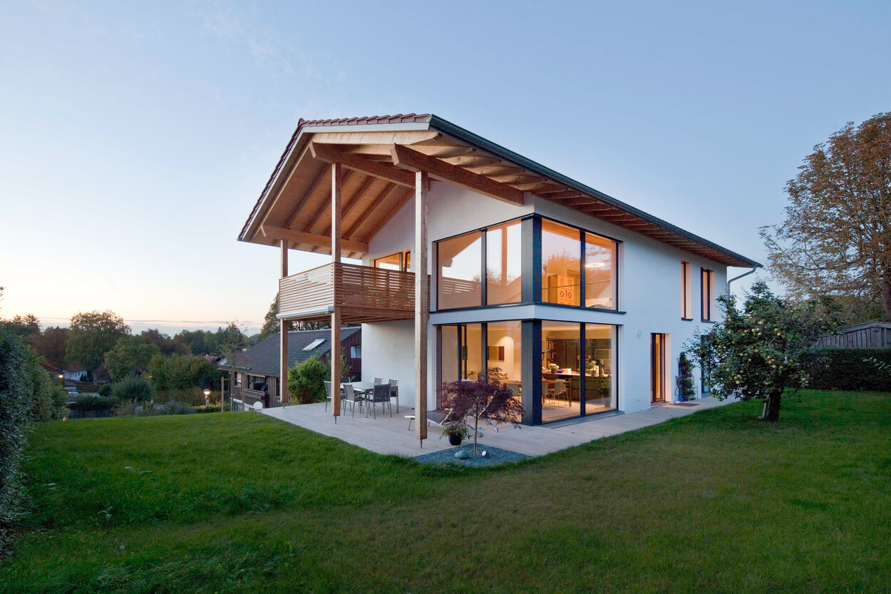 Ein modernes Passivhaus mit großen Glasfronten steht in Oberhaching in einem grünen Garten bei Sonnenuntergang.