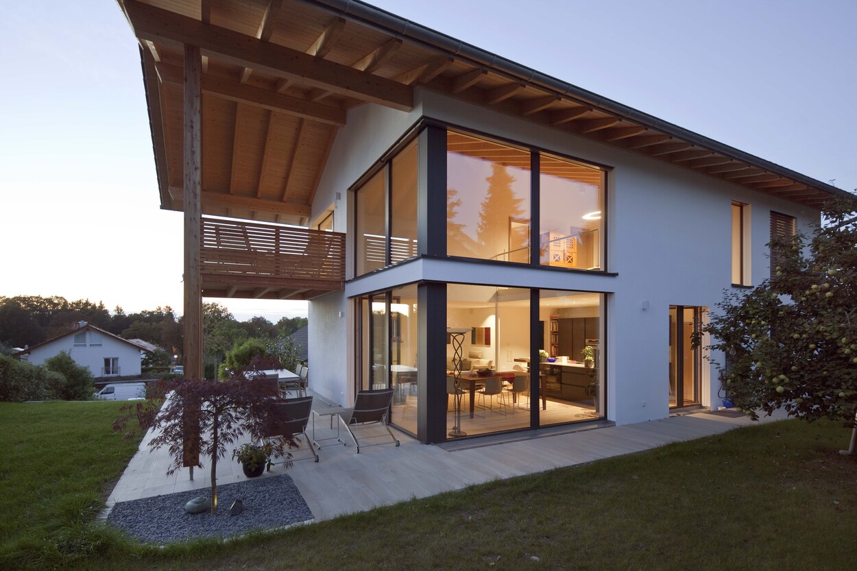 Ein modernes Passivhaus in Oberhaching mit großen Fenstern und Balkon erstrahlt bei Dämmerung im warmen Licht.