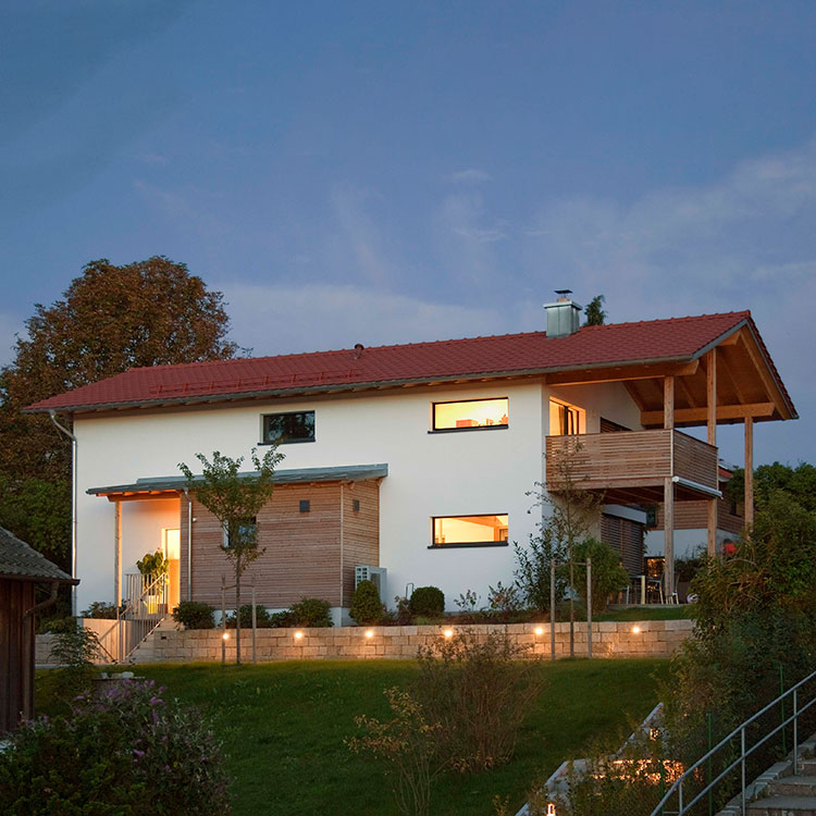 Ein modernes Passivhaus in Oberhaching leuchtet abends, umgeben von einem gepflegten Garten vor einem klaren Himmel.