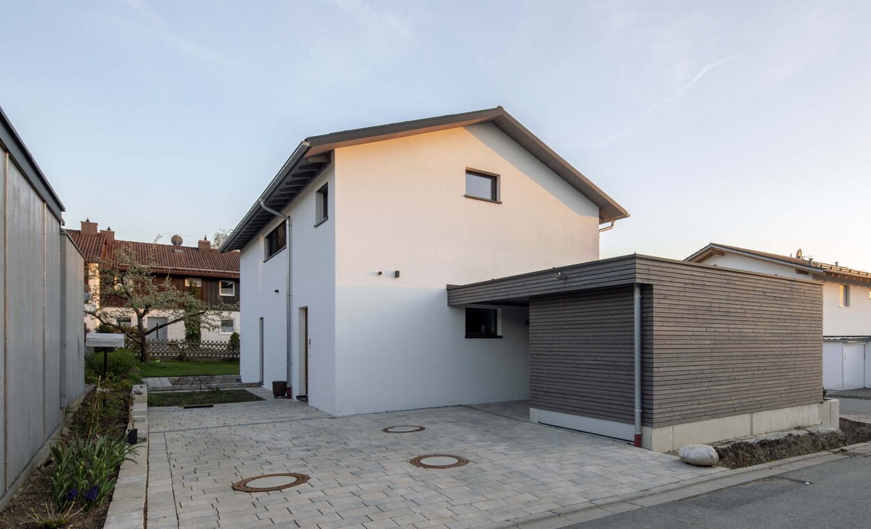 Ein modernes Passivhaus in Andechs präsentiert sich mit schlichter, energieeffizienter Außenansicht und Carport bei Tageslicht.