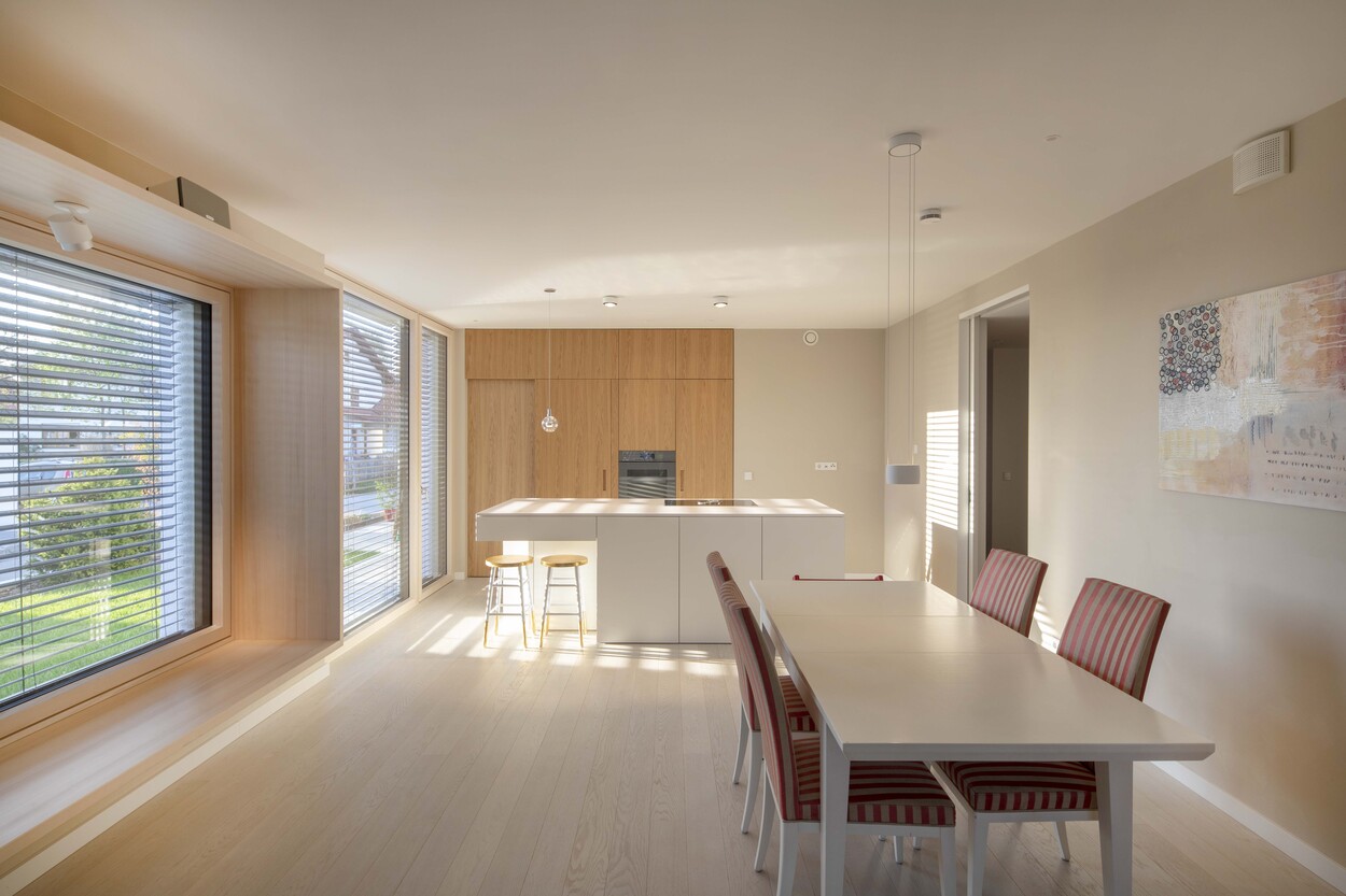 Die moderne Küche im Passivhaus in Andechs strahlt durch große Fenster viel natürliches Licht auf den Esstisch.