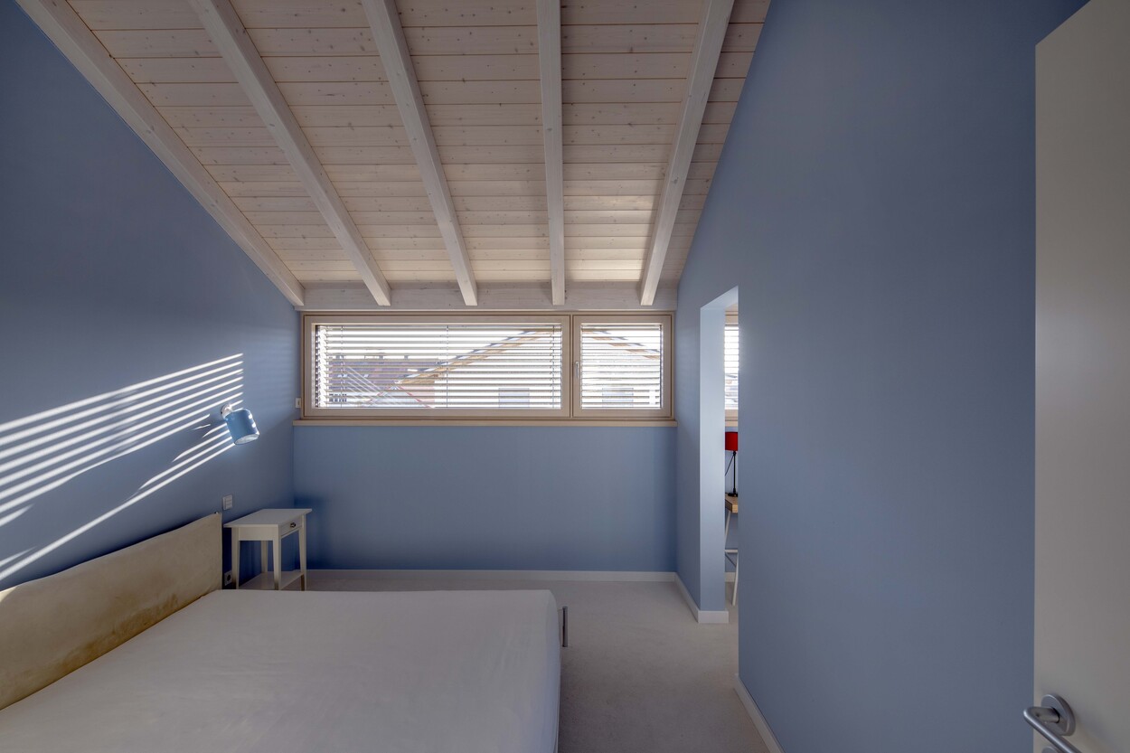 Ein helles Schlafzimmer im Passivhaus-Stil in Andechs, mit blauen Wänden und einem großen Fenster mit Jalousien.