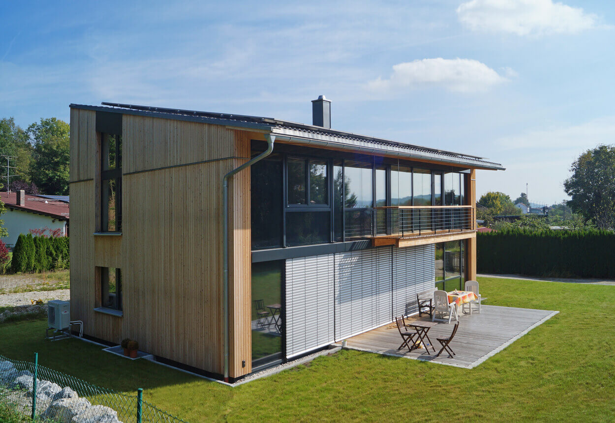 Ein modernes Holz-Einfamilienhaus in Feldkirchen mit großer Glasfront und Terrasse steht in einem gepflegten Garten.