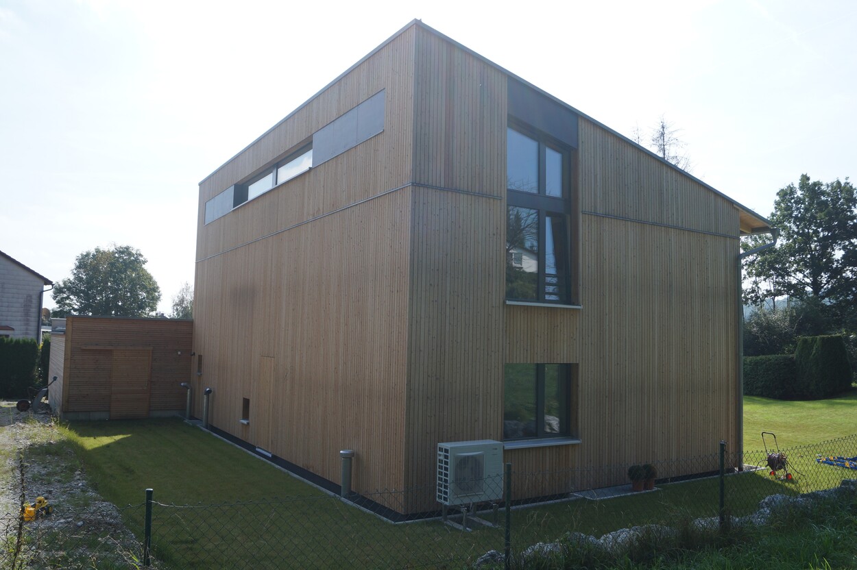Ein modernes Einfamilienhaus aus Holz steht auf einem gepflegten Rasen in Feldkirchen, umgeben von grüner Landschaft.