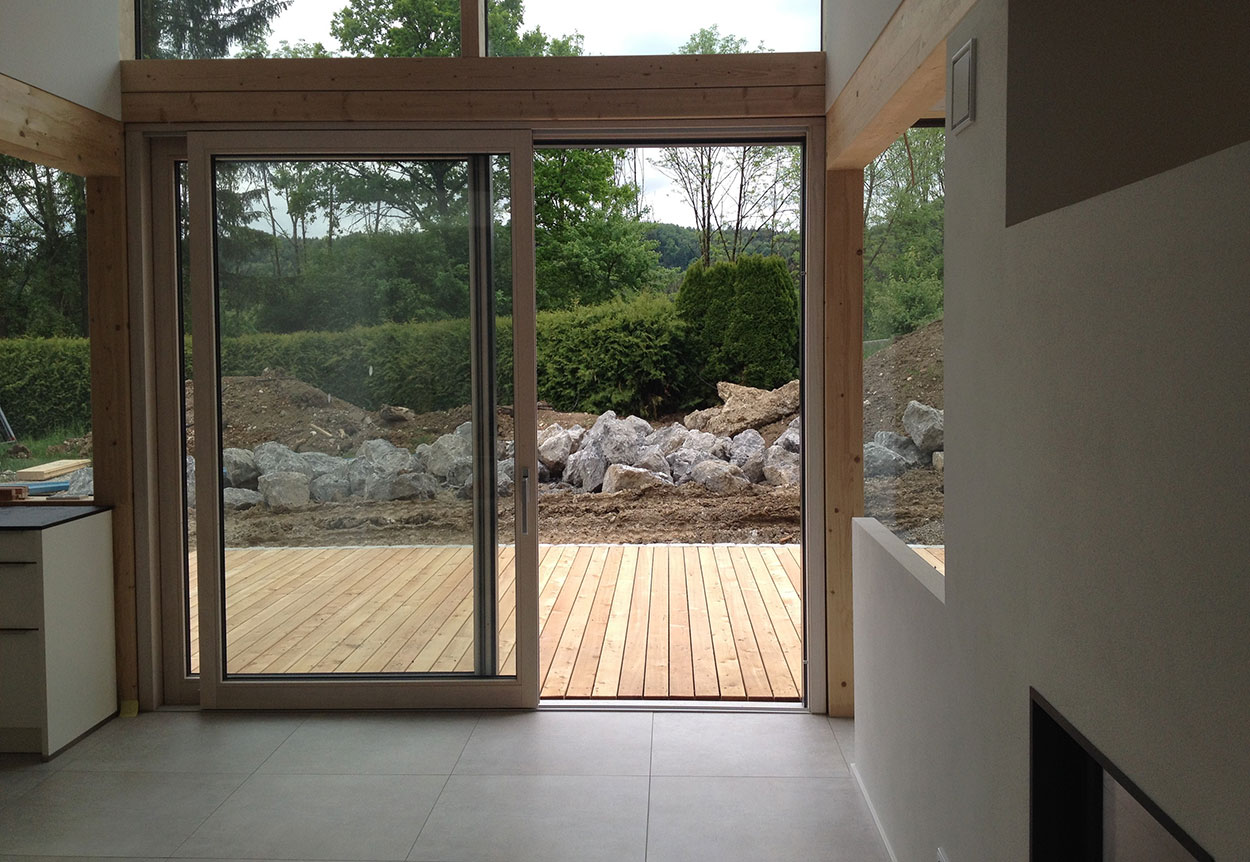 Ein modernes Einfamilienhaus in Holzbauweise öffnet sich mit großen Fenstern zur Terrasse und einem Steingarten in Feldkirchen.