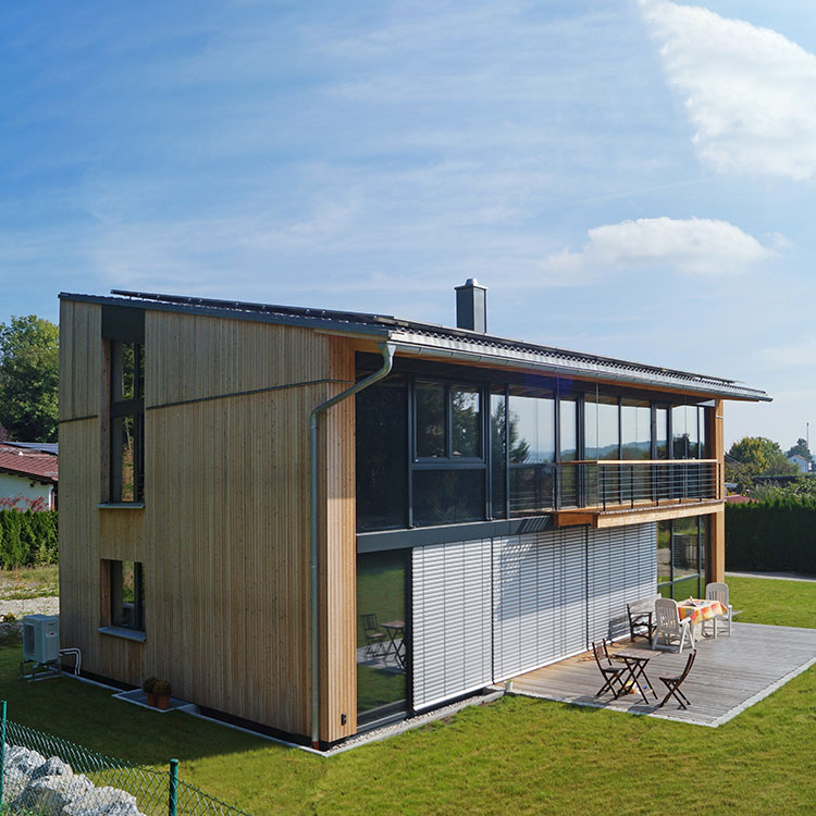 Ein modernes Einfamilienhaus in Holzbauweise steht in Feldkirchen auf einem gepflegten Rasen mit einer sonnigen Terrasse.