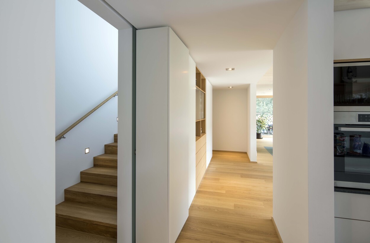 Der Flur eines modernen Passivhauses in München zeigt eine elegante Holztreppe und minimalistische Einbauschränke.