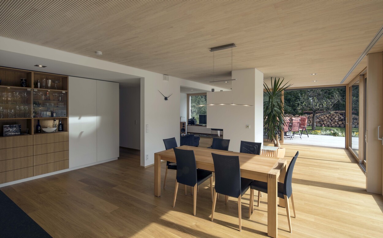 Ein modernes Esszimmer in einem Münchner Passivhaus mit Holzfußboden und großen Fenstern zur Terrasse.