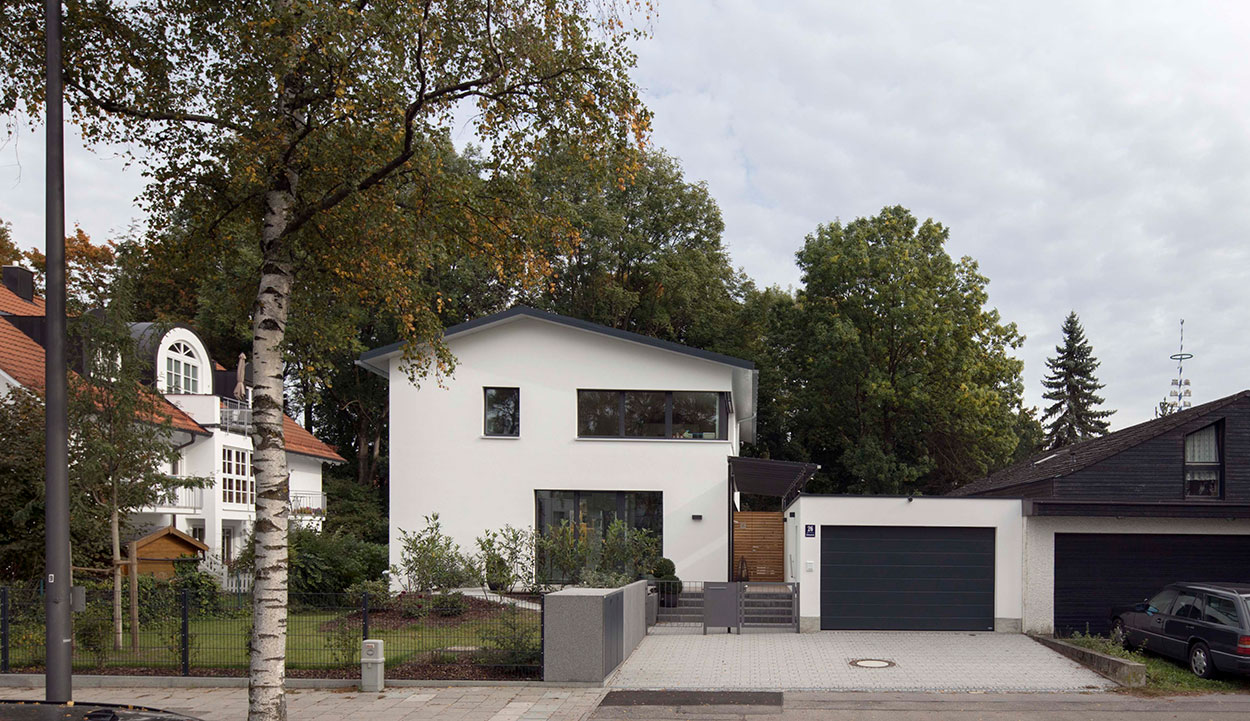 Ein modernes Passivhaus mit großer Garage befindet sich in einer ruhigen, von Bäumen umgebenen Wohngegend in München.
