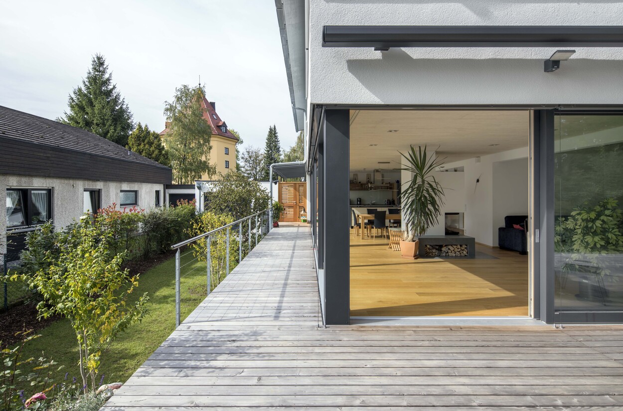 Eine moderne Terrasse eines Passivhauses in München führt zu einem offenen Wohnbereich mit großen, lichtdurchfluteten Fenstern.