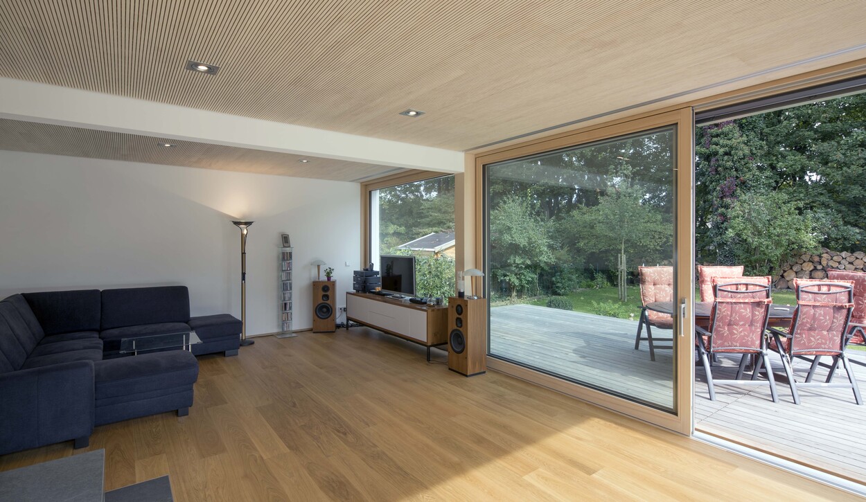 Ein modernes Wohnzimmer in einem Passivhaus in München öffnet sich durch große Fenster zur Terrasse mit stilvollen Sitzmöbeln.