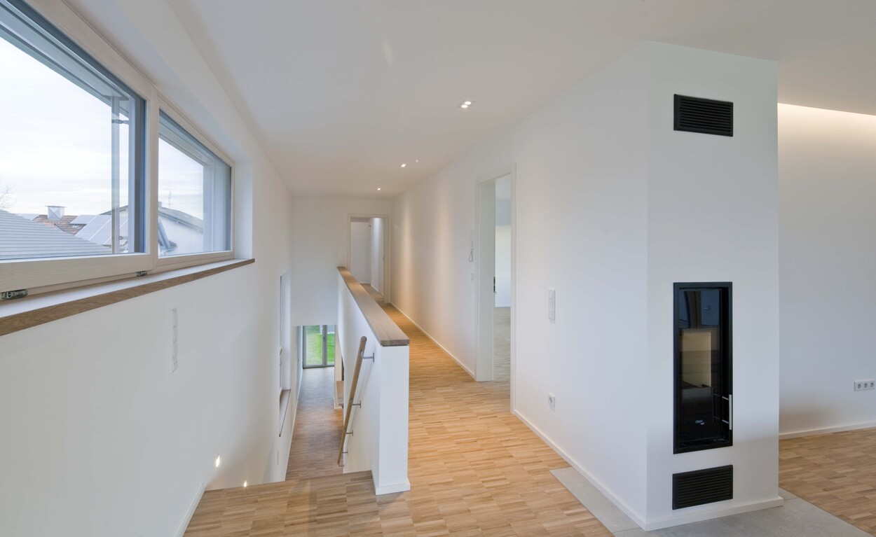 Ein heller Flur mit Holzboden und großen Fenstern erstreckt sich in einem modernen Passivhaus in Bruckmühl.