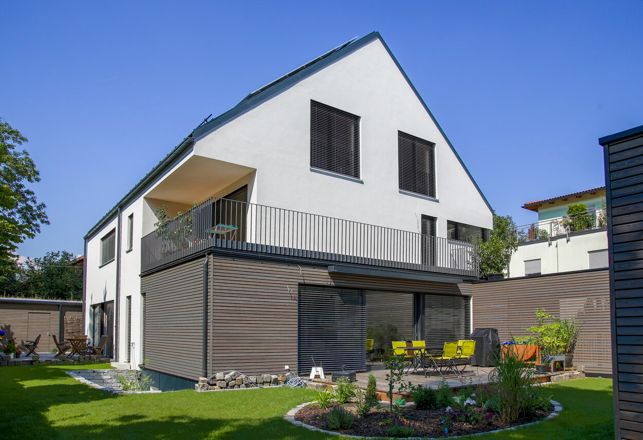 Ein modernes Passivhaus-Doppelhaus in München mit Terrasse und Garten erstrahlt unter blauem Himmel.