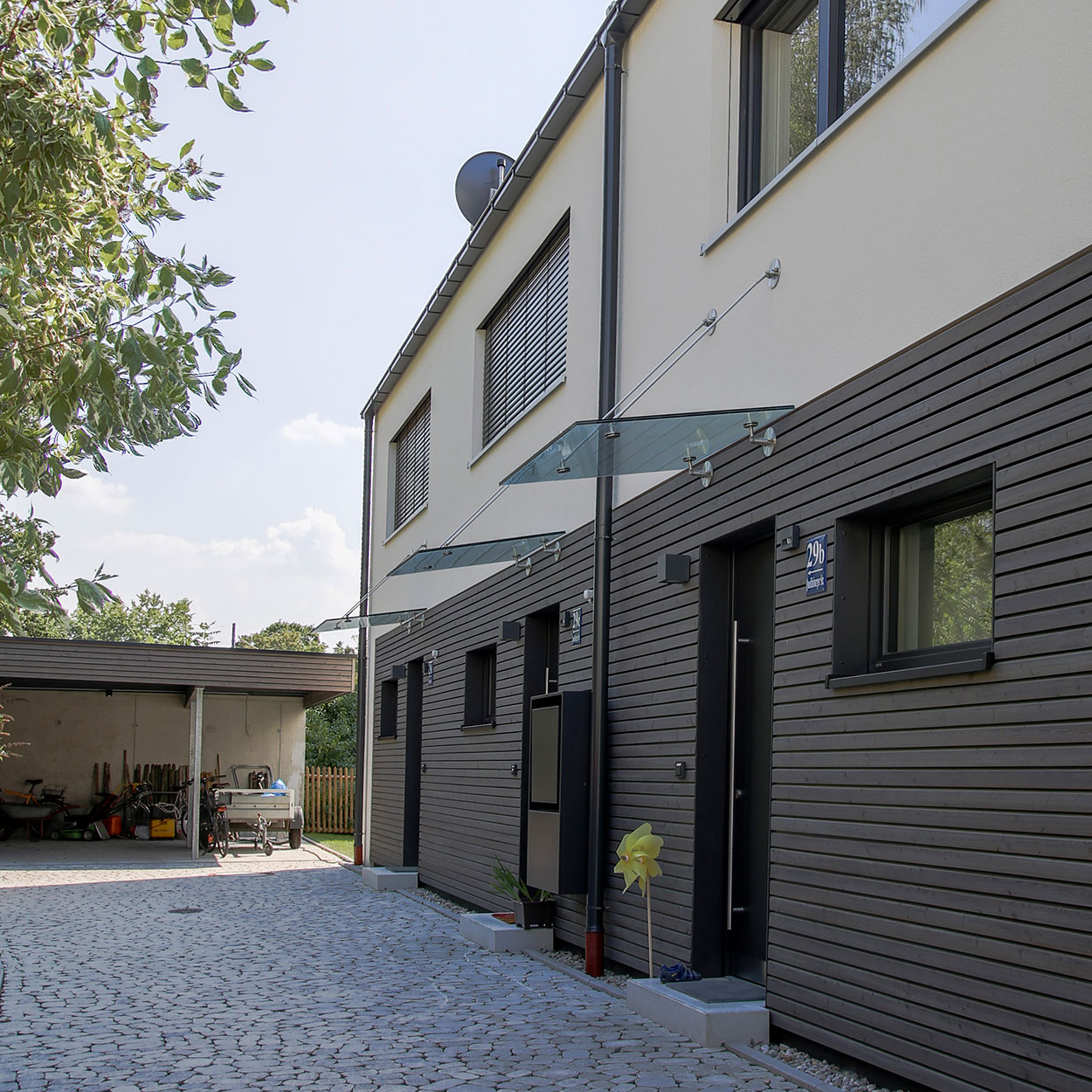 Der Eingang eines modernen Passiv-Doppelhauses in München zeigt stilvolle Glasvordächer und eine gepflegte gepflasterte Einfahrt.