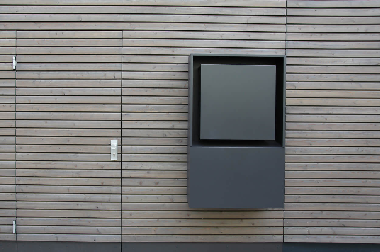 Die Fassade eines Doppelhauses in München zeigt moderne Holzverkleidung mit einem grauen Kasten als Designelement.