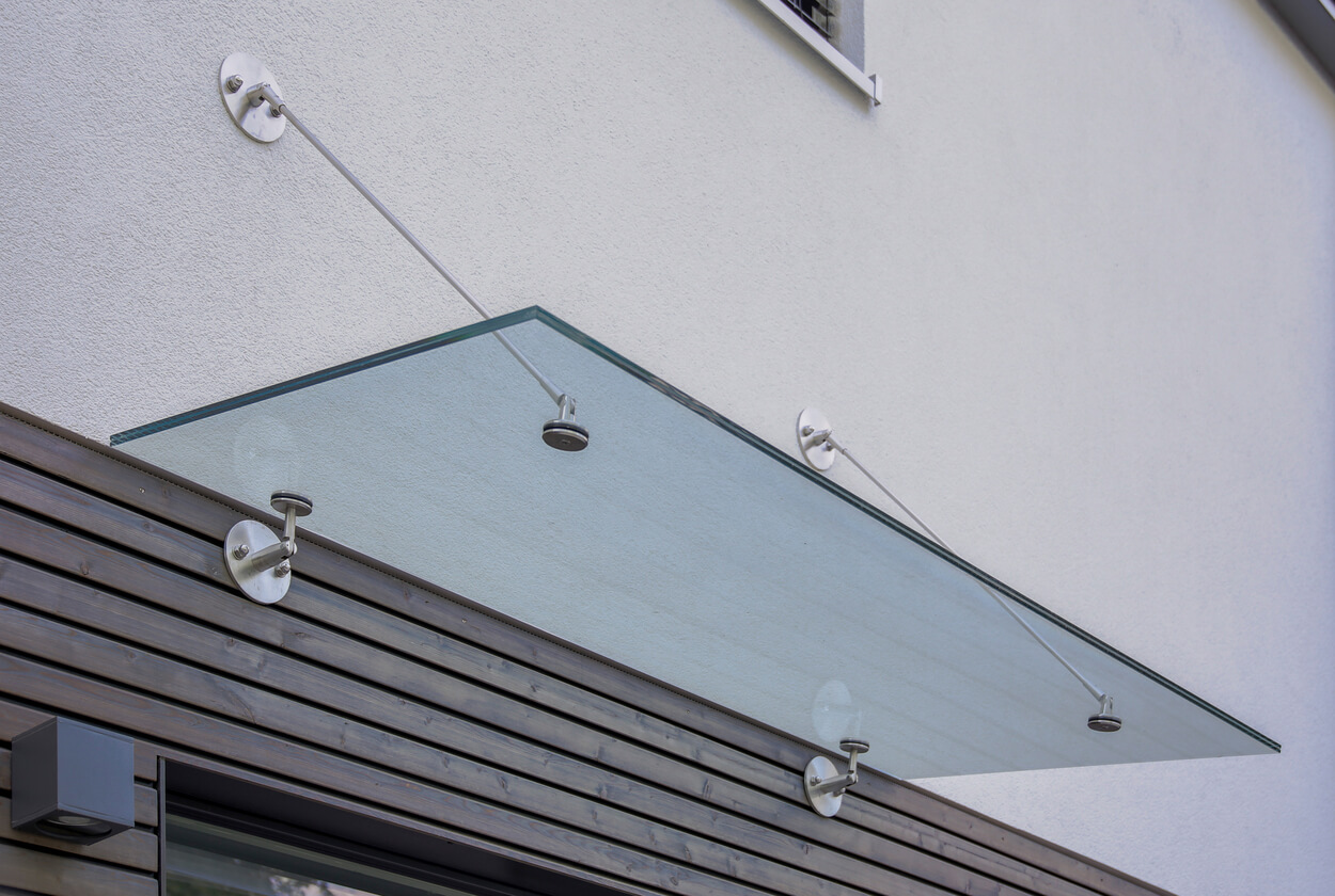 Ein modernes Glasvordach bietet stilvollen Wetterschutz an der Fassade eines Passivhauses in München.