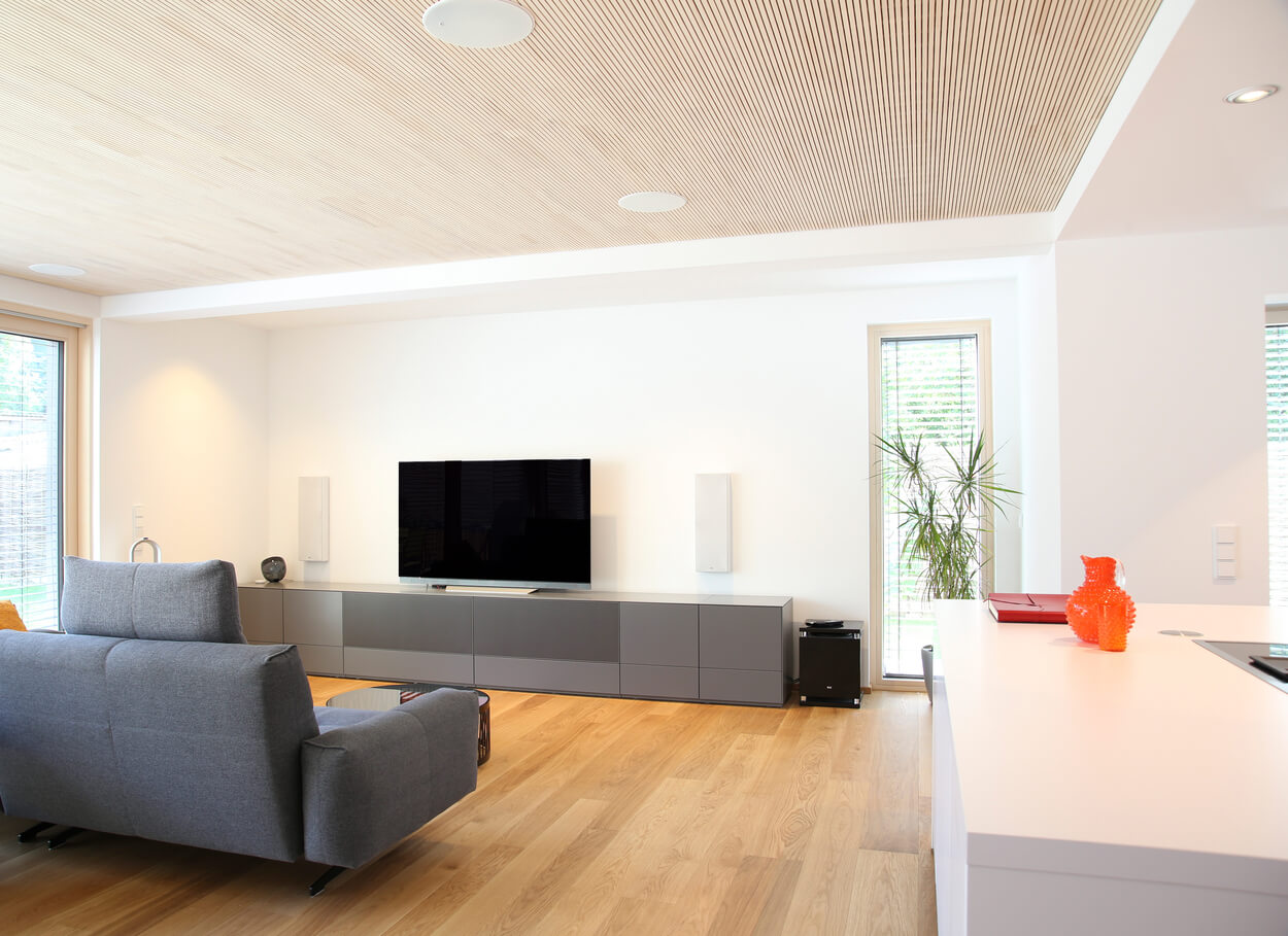 Modernes Wohnzimmer in einem Doppelhaus-Passivhaus in München mit grauem Sofa, Holzboden und großem Fernseher.