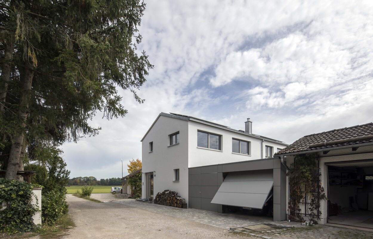 Ein modernes Energiesparhaus in Putzbrunn mit einer offenen Garage und Holzstapeln, unter einem bewölkten Himmel.