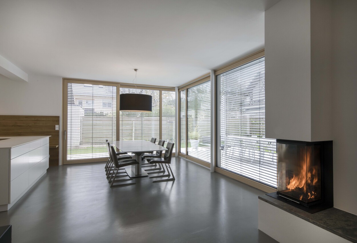Ein modernes Esszimmer in einem energiesparenden Holzhaus mit großen Fenstern, elegantem Esstisch und brennendem Kamin.