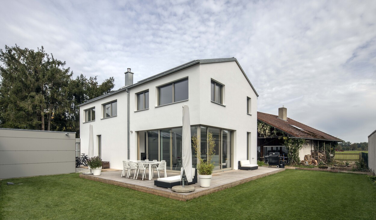 Ein modernes energiesparendes Holzhaus in Putzbrunn mit großer Terrasse und grünem Garten unter bewölktem Himmel.