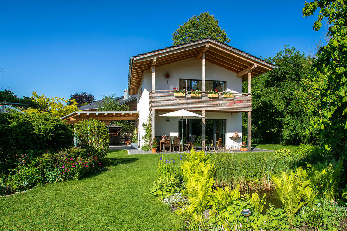 Ein modernes Passivhaus in Bad Aibling thront im üppigen Garten, umrahmt von strahlend blauem Himmel.