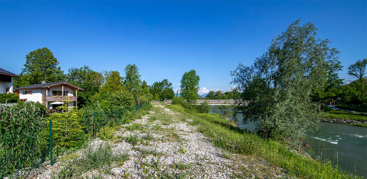 Ein modernes Passivhaus steht in Bad Aibling neben einem Fluss, umgeben von üppiger Natur und klarem Himmel.