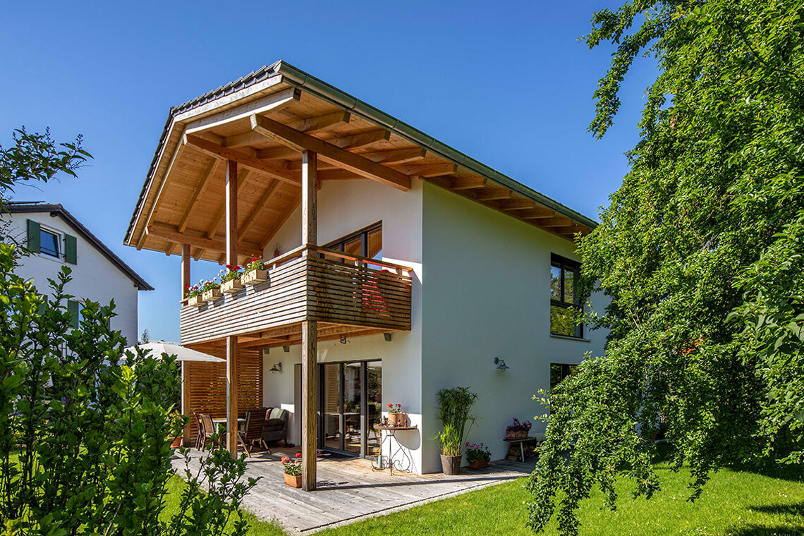 Ein modernes Passivhaus in Bad Aibling mit großzügigem Balkon und üppigem Garten bei strahlendem Sonnenschein.