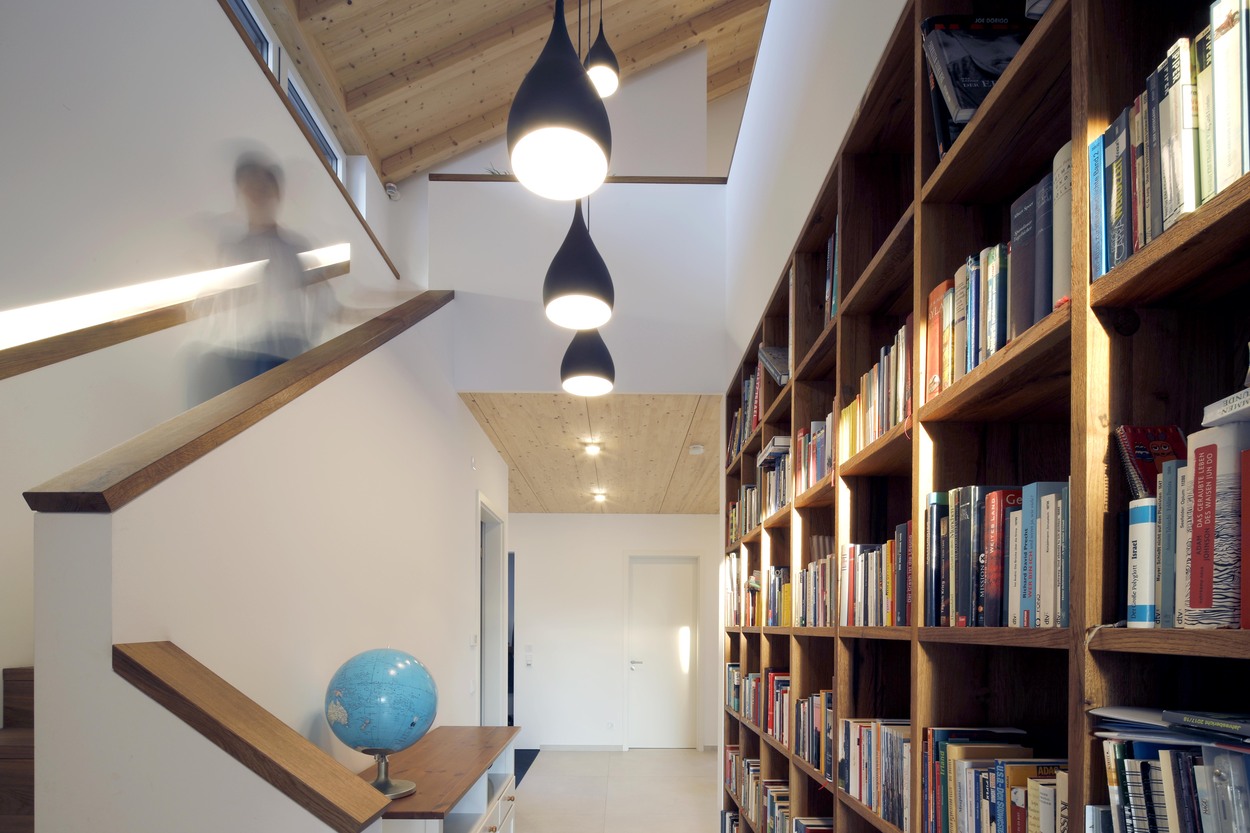 Eine Person geht eine Treppe im modernen Holzhaus hinunter, vorbei an einer großen Bücherwand und einem blauen Globus.