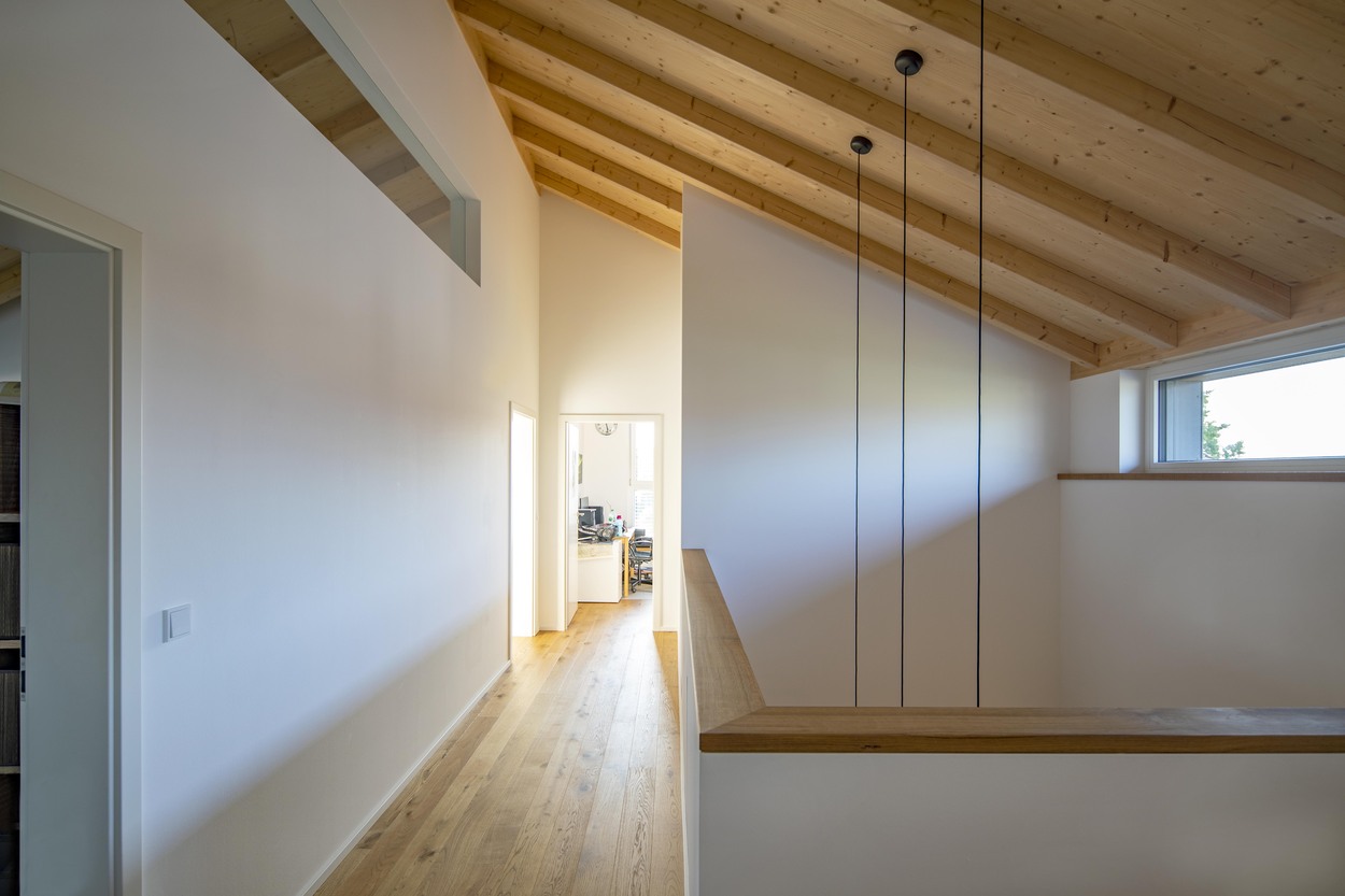 Ein modernes Holzhaus in Oberpframmern zeigt einen lichtdurchfluteten Flur mit Holzdecke und hellem Parkettboden.