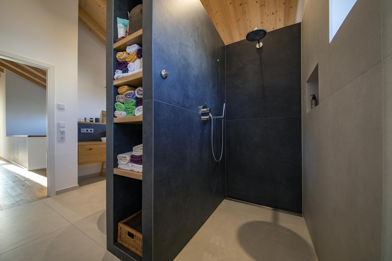 Eine moderne Dusche in einem Holzhaus mit eleganten dunklen Wänden und offenen Regalen voller bunter Handtücher.